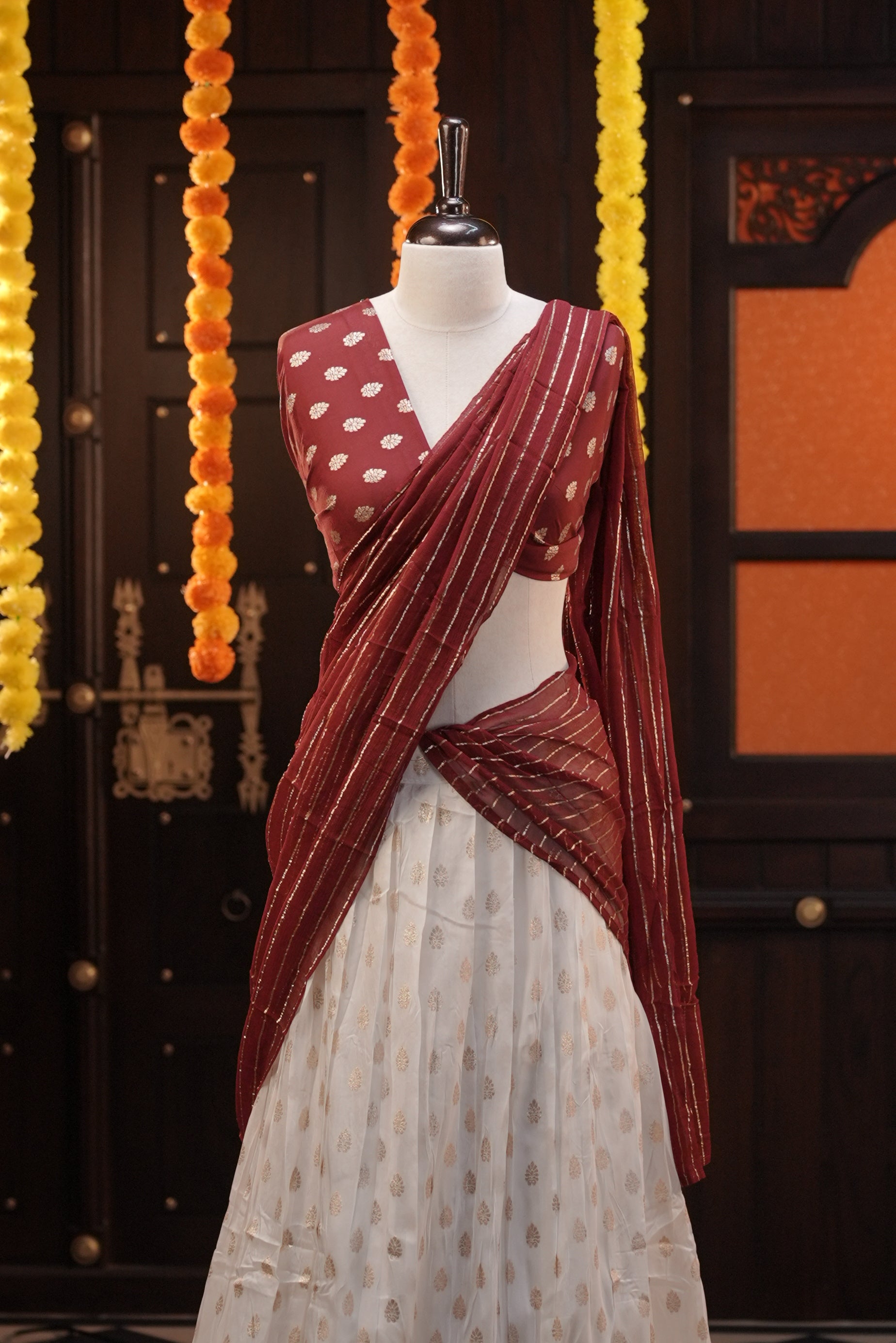 Off white colour Semi Stitched Banaras Dhavani Set Featuring off white Skirt with Gold zari buttas & Traditional border, paired with Maroon colour Blouse material with gold zari buttas, finishing with same colour with gold zari Stripped Dupatta.
