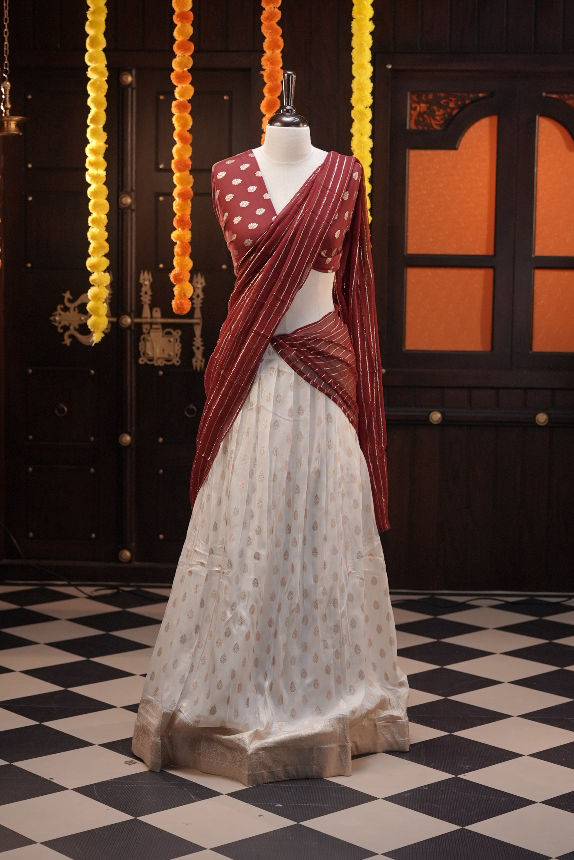 Off white colour Semi Stitched Banaras Dhavani Set Featuring off white Skirt with Gold zari buttas & Traditional border, paired with Maroon colour Blouse material with gold zari buttas, finishing with same colour with gold zari Stripped Dupatta.