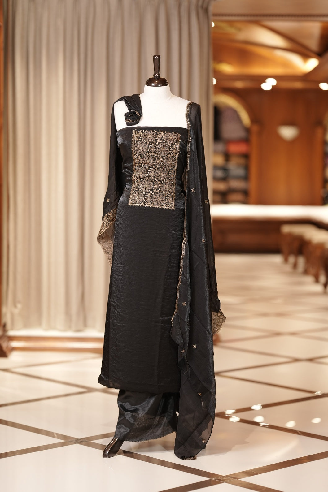 Black colour Semi silk Salwar suit featuring rich golden zari and sequin work on the floral designed neckline, scallop border, and delicate floral motifs on the dupatta & paired with a plain bottom.