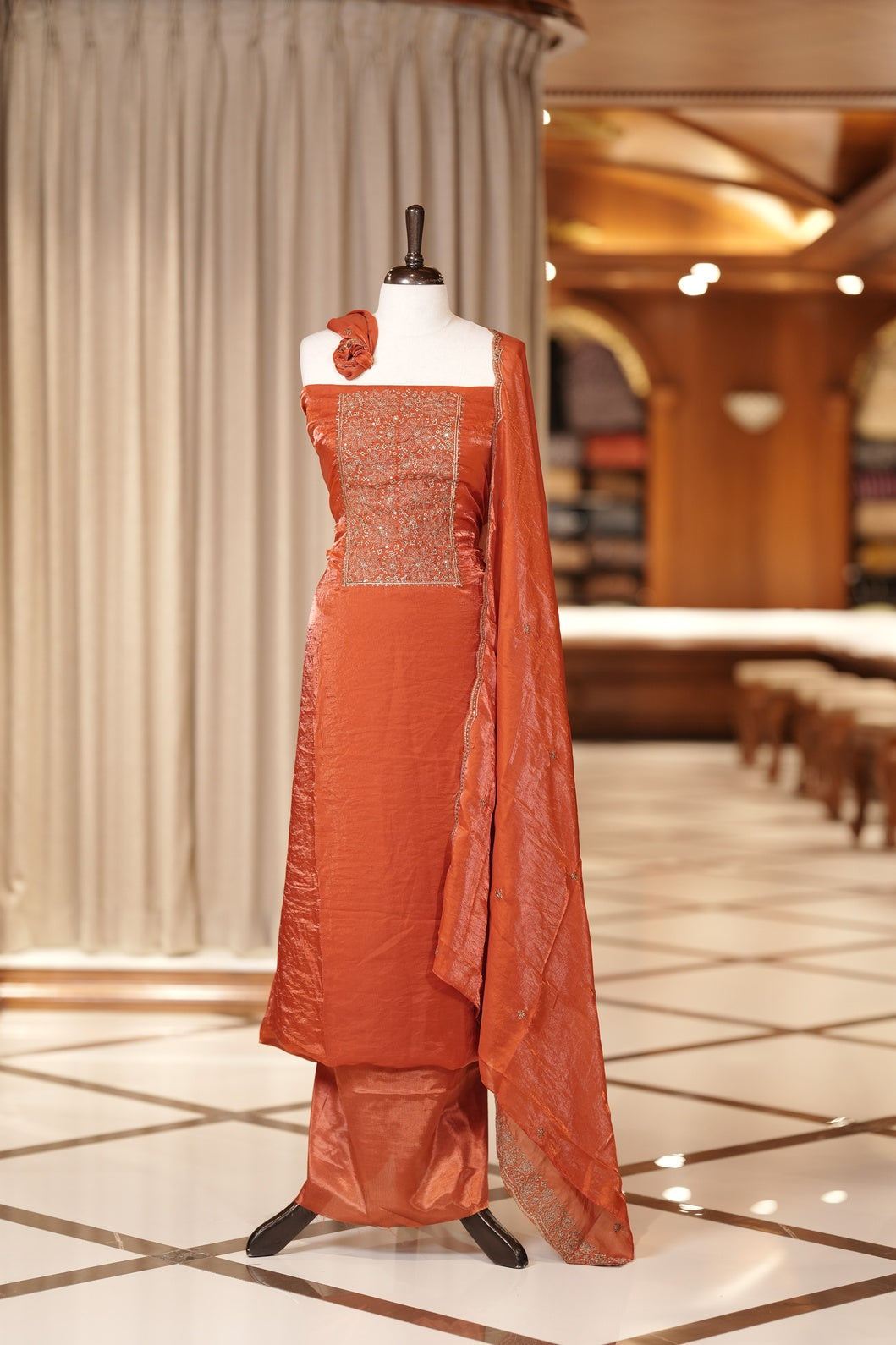 Orange colour Semi silk Salwar suit featuring rich golden zari and sequin work on the floral designed neckline, scallop border, and delicate floral motifs on the dupatta & paired with a plain bottom.