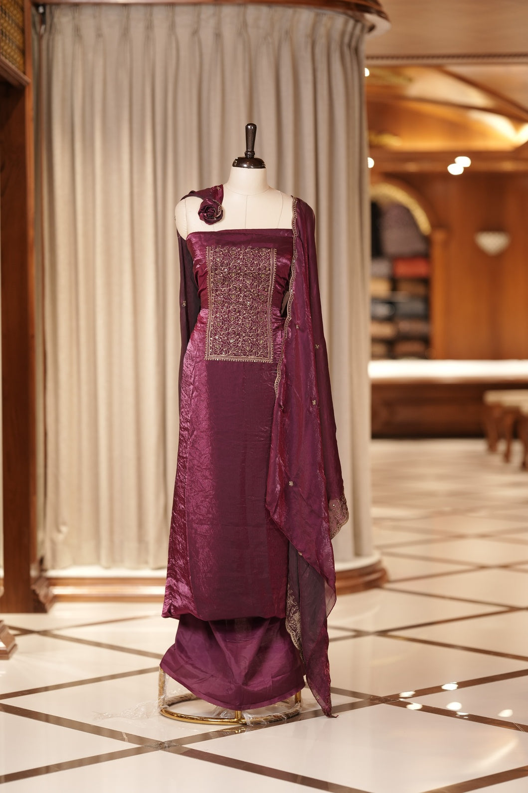 Wine colour Semi silk Salwar suit featuring rich golden zari and sequin work on the floral designed neckline, scallop border, and delicate floral motifs on the dupatta & paired with a plain bottom.