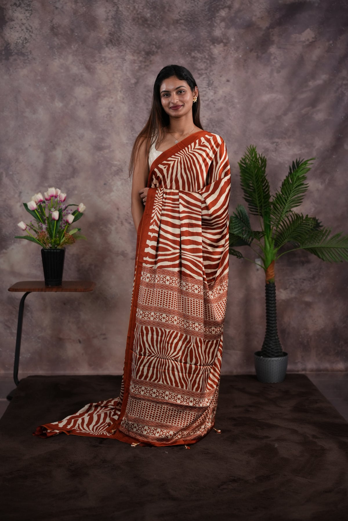 Rust Orange Colour satin model saree featuring Zibra print on body. Ajrak & zibra print on pallu with jhumka tassels, comes with contrast plain blouse piece.