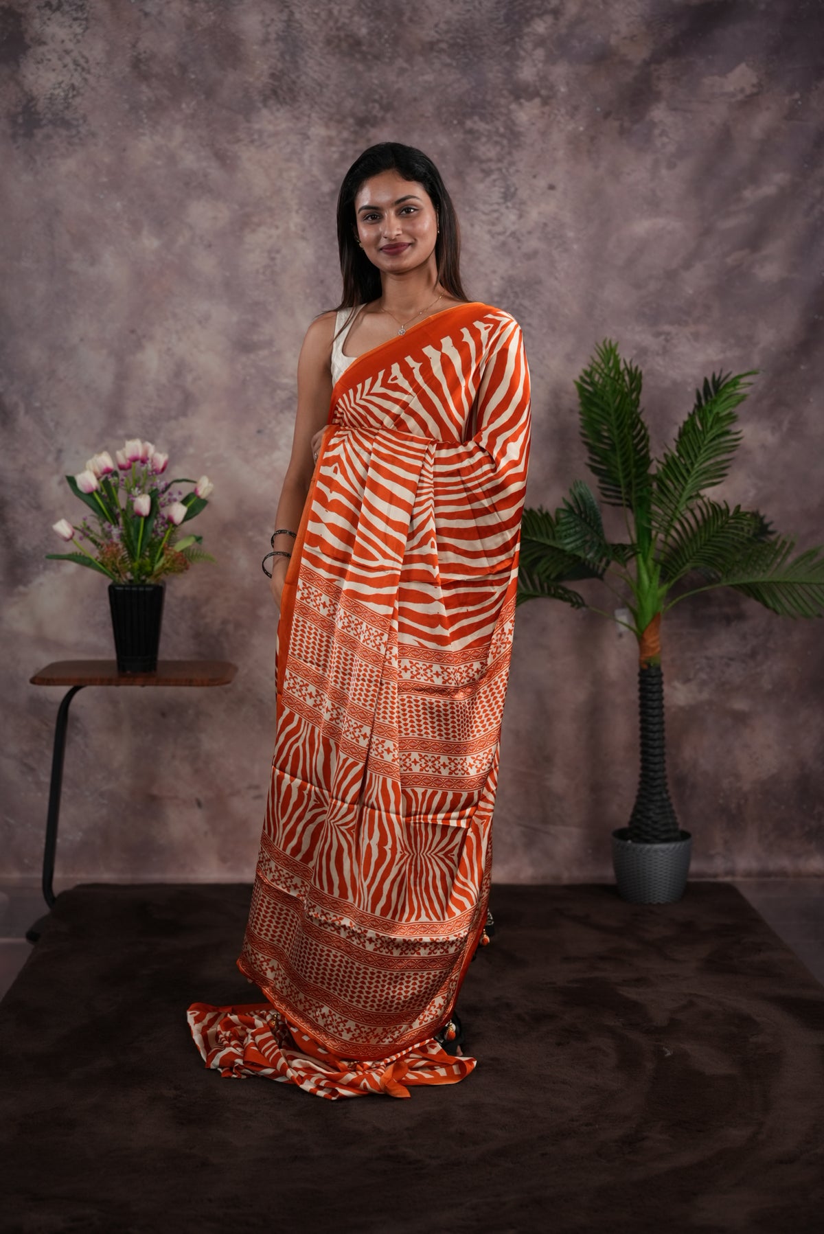 Orange Colour satin model saree featuring Zibra print on body. Ajrak & zibra print on pallu with jhumka tassels, comes with contrast plain blouse piece.