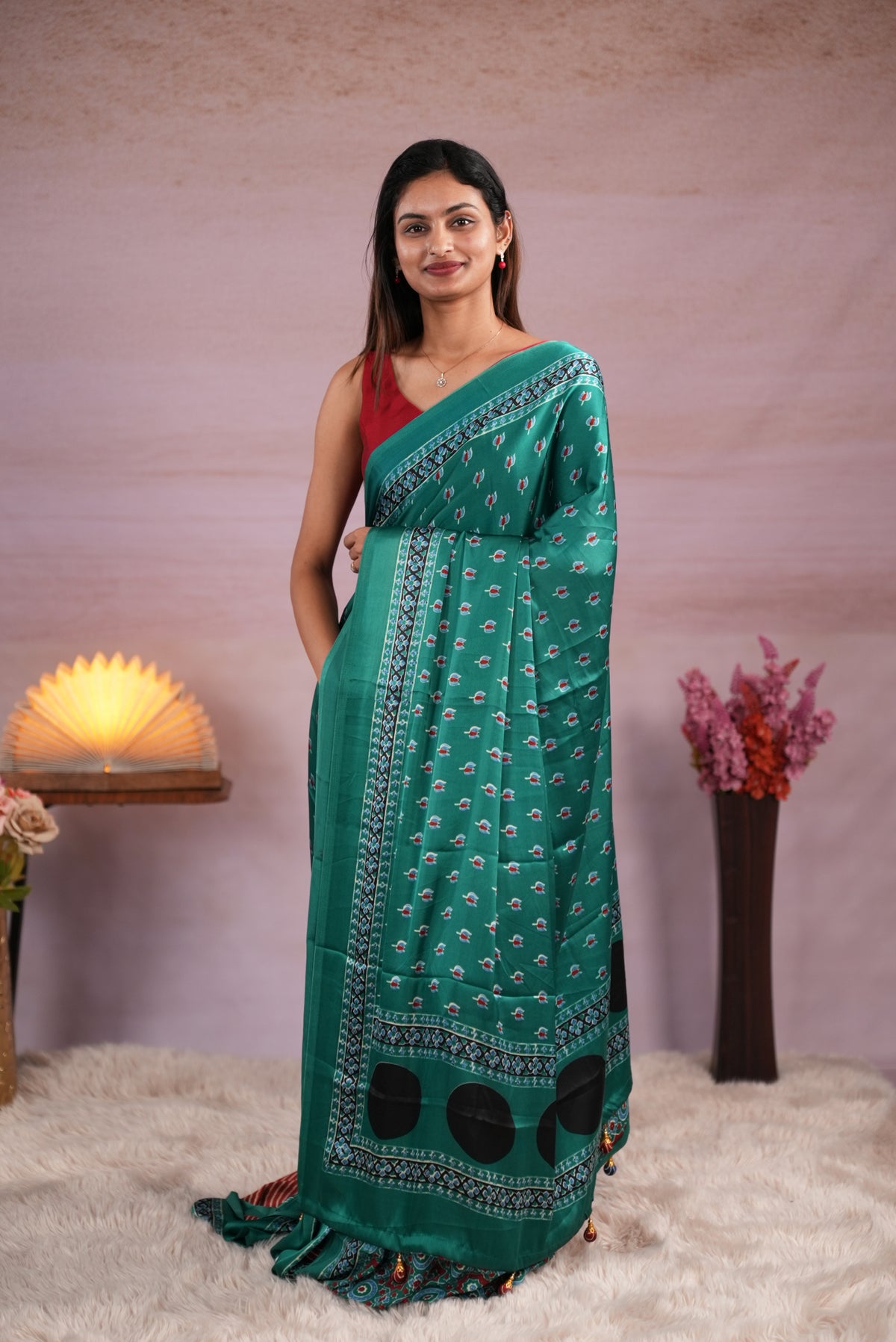 Peacock Green and Rust Orange colour satin modal saree featuring stripes on the body, Ajrakh prints on the border & polka dots with jhumka tassels on the pallu, paired with a matching Ajrakh printed blouse piece.