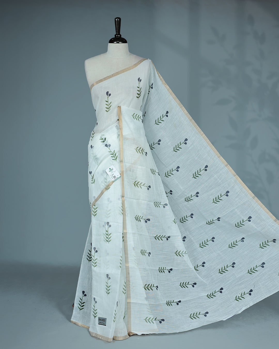 Off-white linen saree featuring beautiful Blue floral and leafy prints on the body, complemented by a tissue piping border and a contrasting pallu. Paired with a matching blouse piece.
