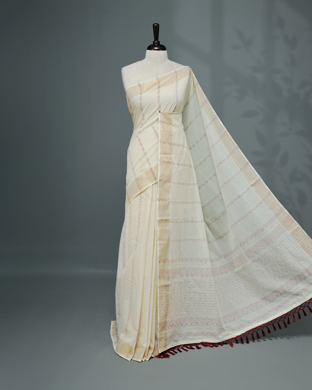 Cream colour Cotton kerala saree featuring Maroon & gold Strips on body, complemented by Gold zari Border, paired with matching blouse piece.