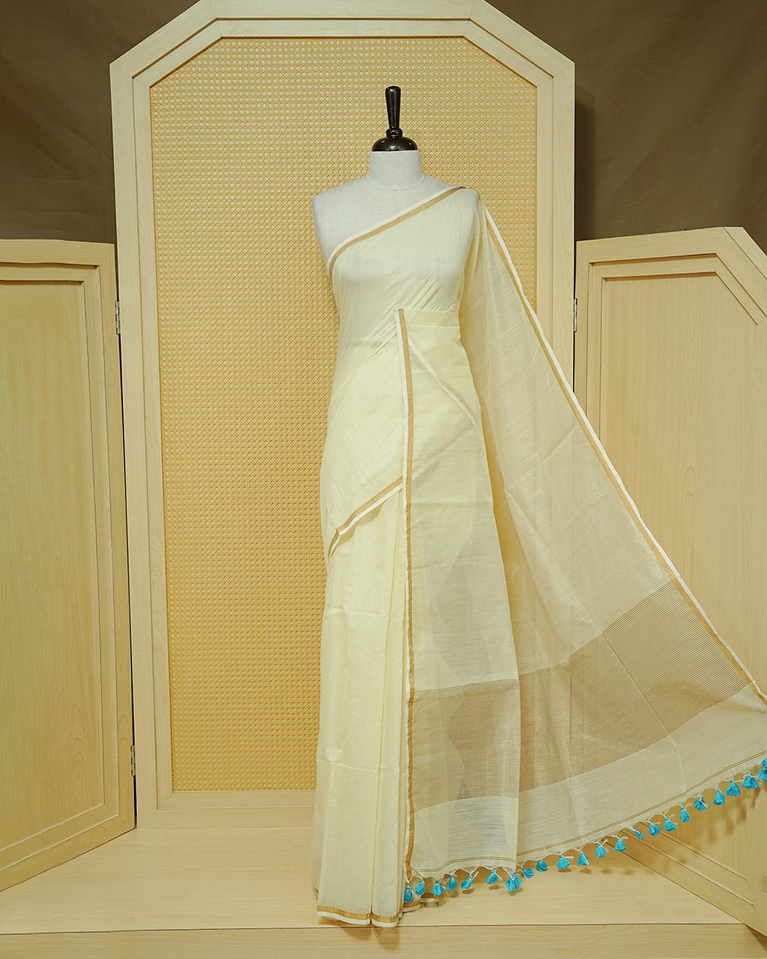 Cream Mul Cotton Saree featuring an elegant plain body, complemented by a subtle gold zari border and sky blue tassels.