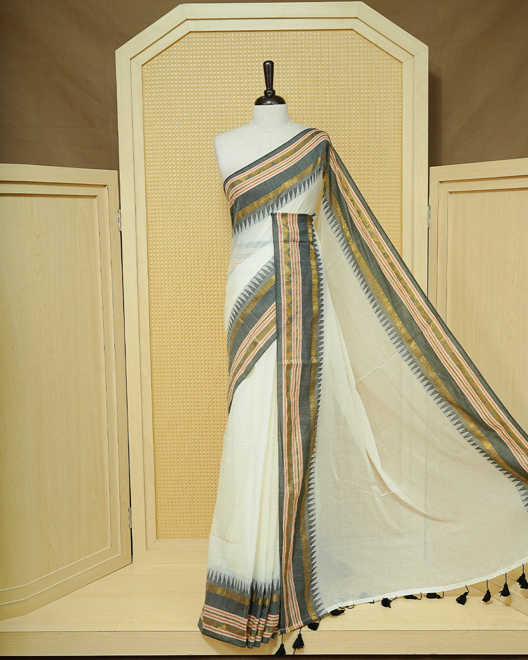 Cream Mul Cotton Saree featuring an elegant plain body, complemented by a grey contrast border with gold zari and subtle Red stripe detailing, finished with black tassels.