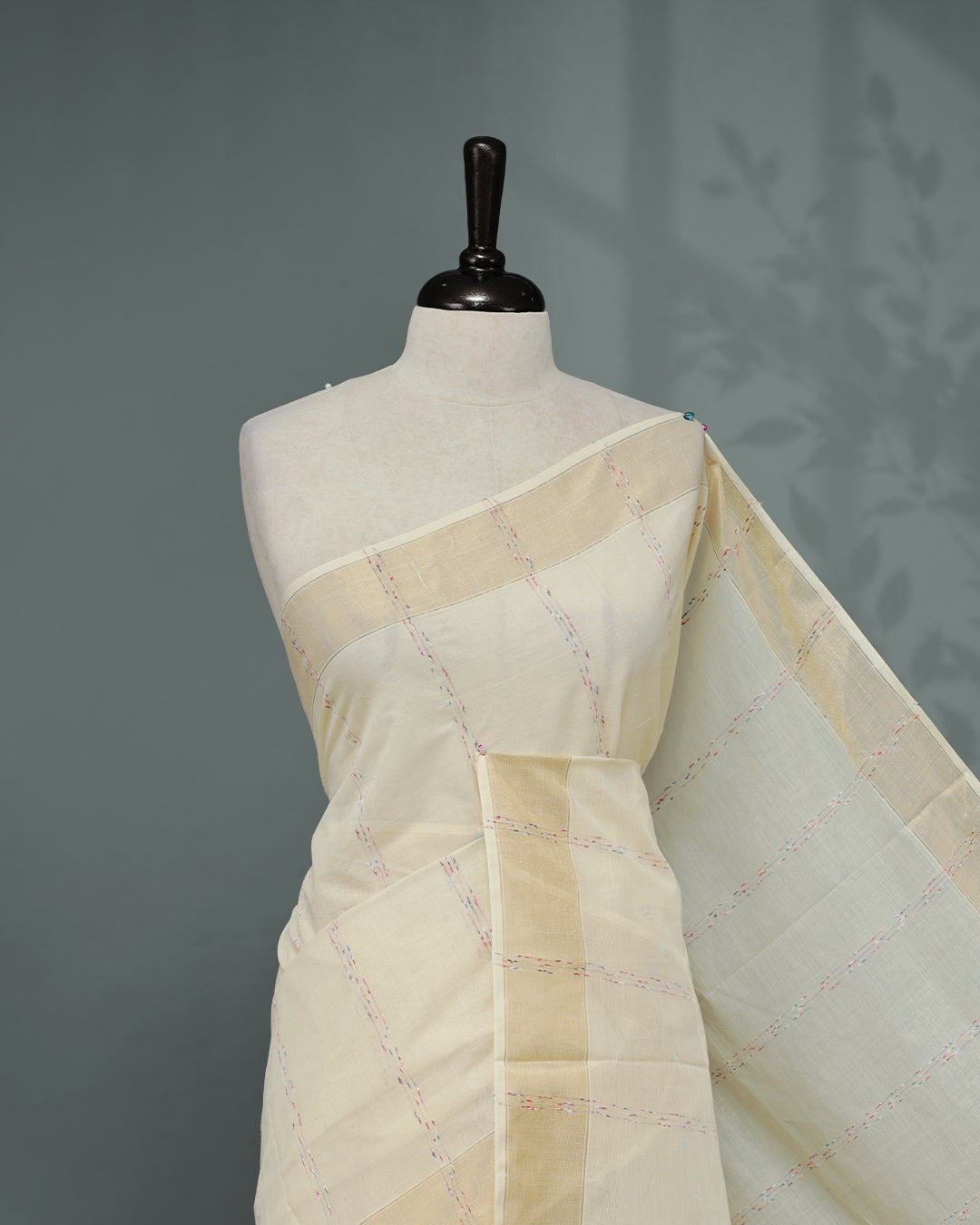 Cream colour Cotton kerala saree featuring Multicolour & gold Strips on body, complemented by Gold zari Border, paired with matching blouse piece.