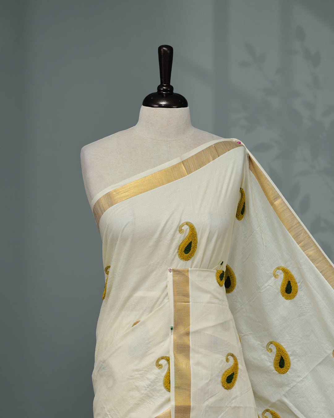 Cream colour Cotton kerala saree featuring Mango Embroidery work on the body, complemented by a gold zari Border, paired with a matching blouse piece.