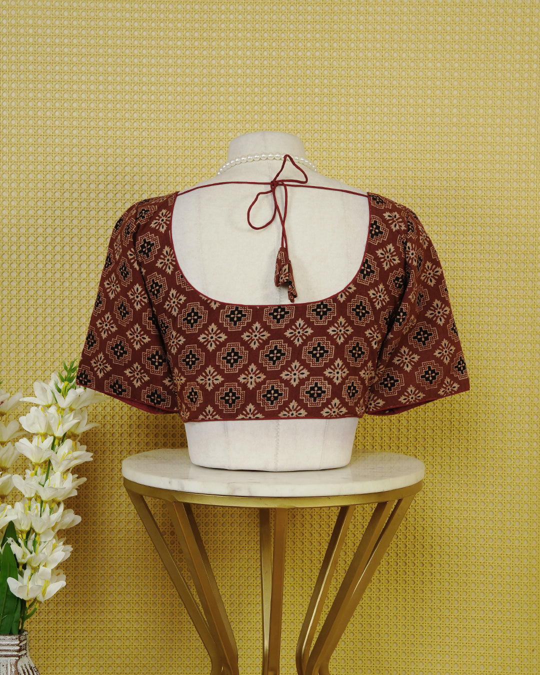 Maroon Colour Printed Blouse Featuring An All Over Geometric Floral Motif, Enhanced With A Round Neckline, Front Button Closure, And Elbow Length Sleeves.