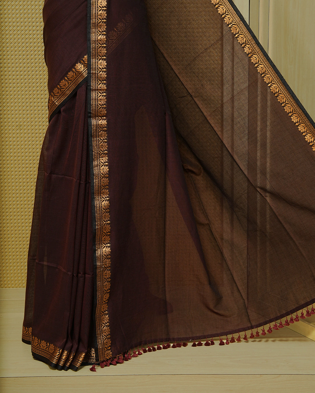 Chocolate brown colour Mul cotton saree featuring an elegant plain body, complemented by self colour with Gold zari border & tassels.