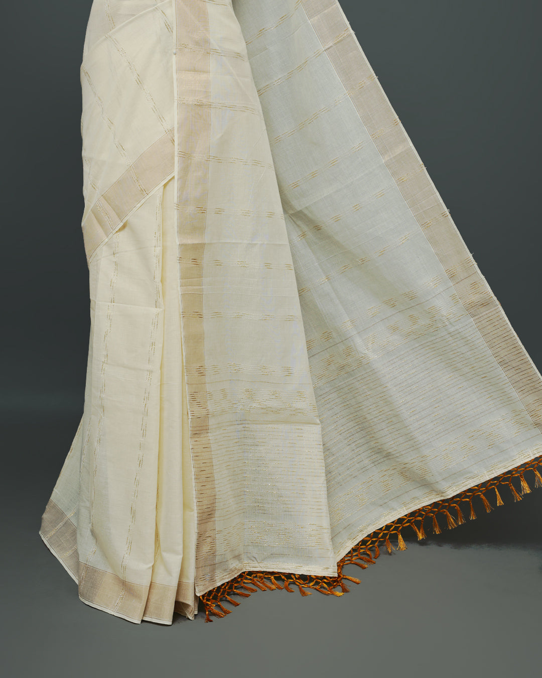 Cream colour Cotton kerala saree featuring Gold Embroidery strips on the body, complemented by a gold zari Border, Yellow elegant tassels, paired with a matching blouse piece.