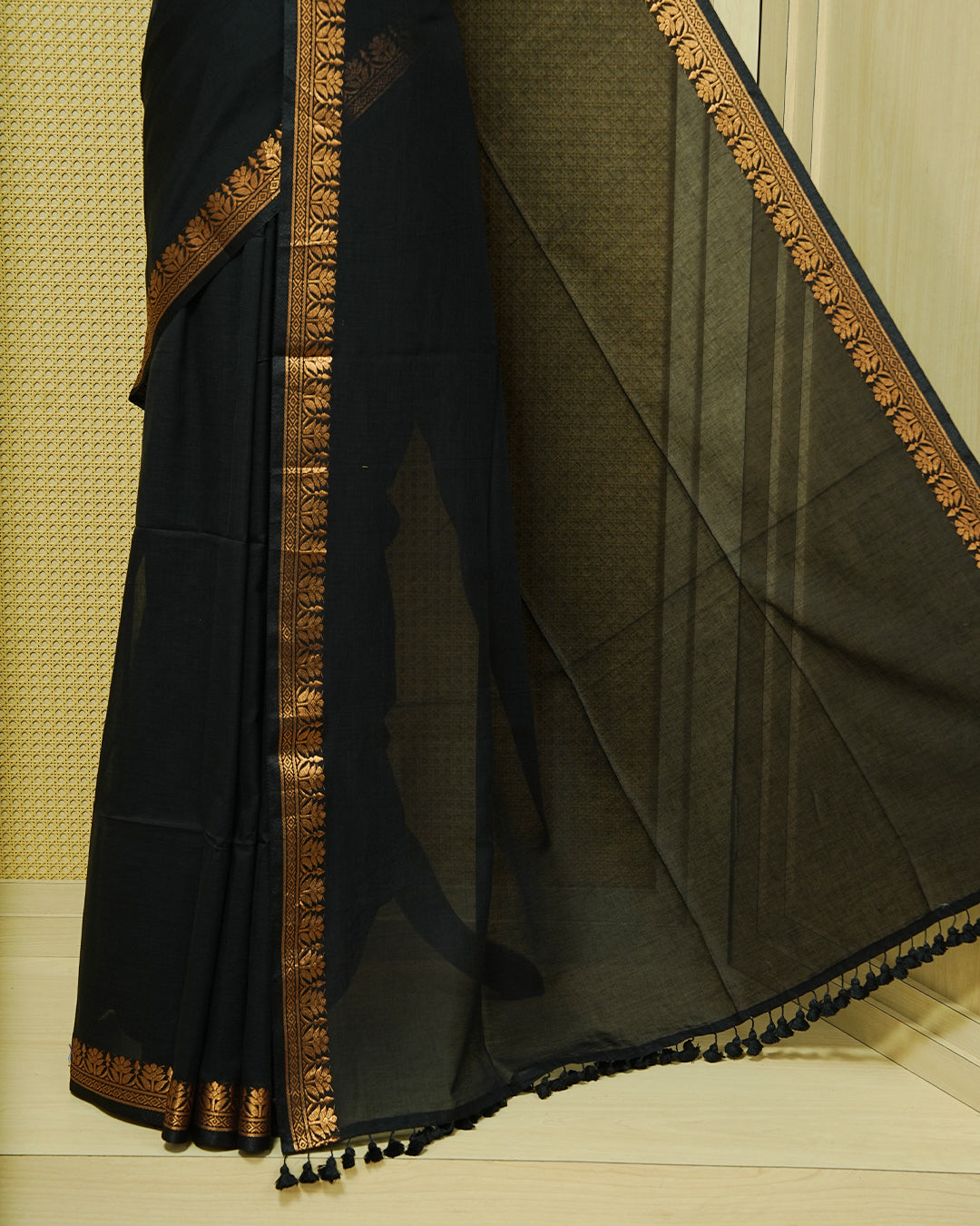 Black Colour Mul Cotton Saree featuring a plain body, complemented by a copper zari border and black tassels.