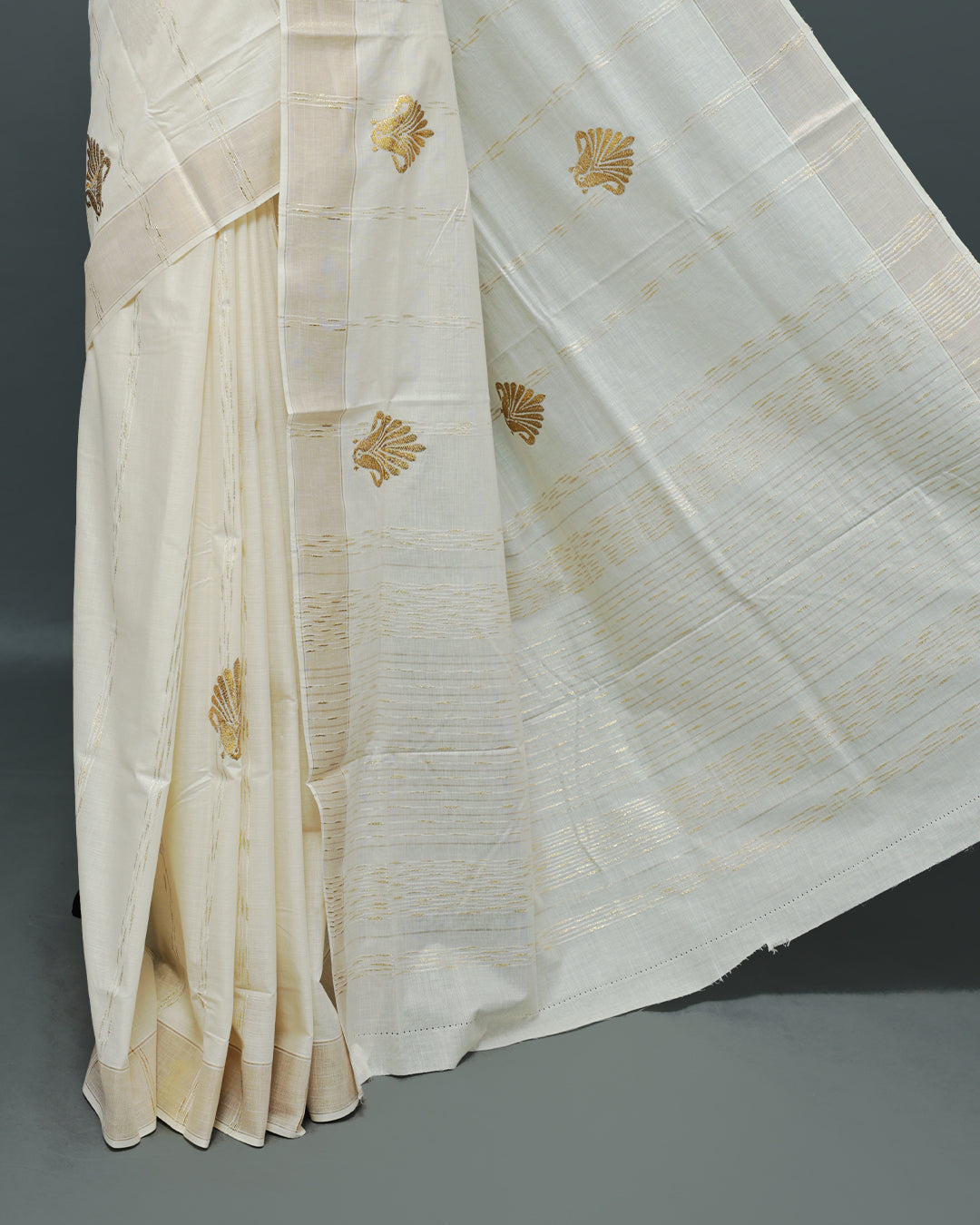 Cream colour Cotton kerala saree featuring Gold Embroidery strips with motifs on the body, complemented by a gold zari Border, paired with a matching blouse piece.