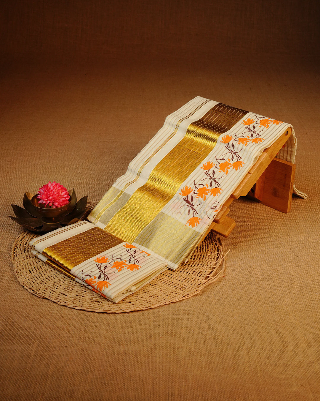 Cream colour Cotton set mundu features a Strip on body accented by a Gold with Orange Floral pattern on border.