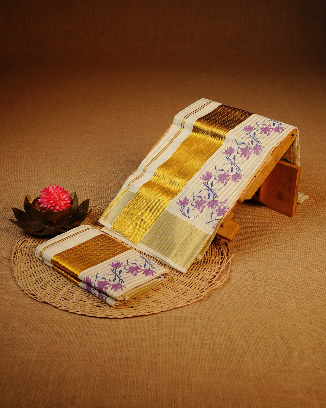 Cream colour Cotton set mundu features a Strip on body accented by a Gold with Purple Floral pattern on border.