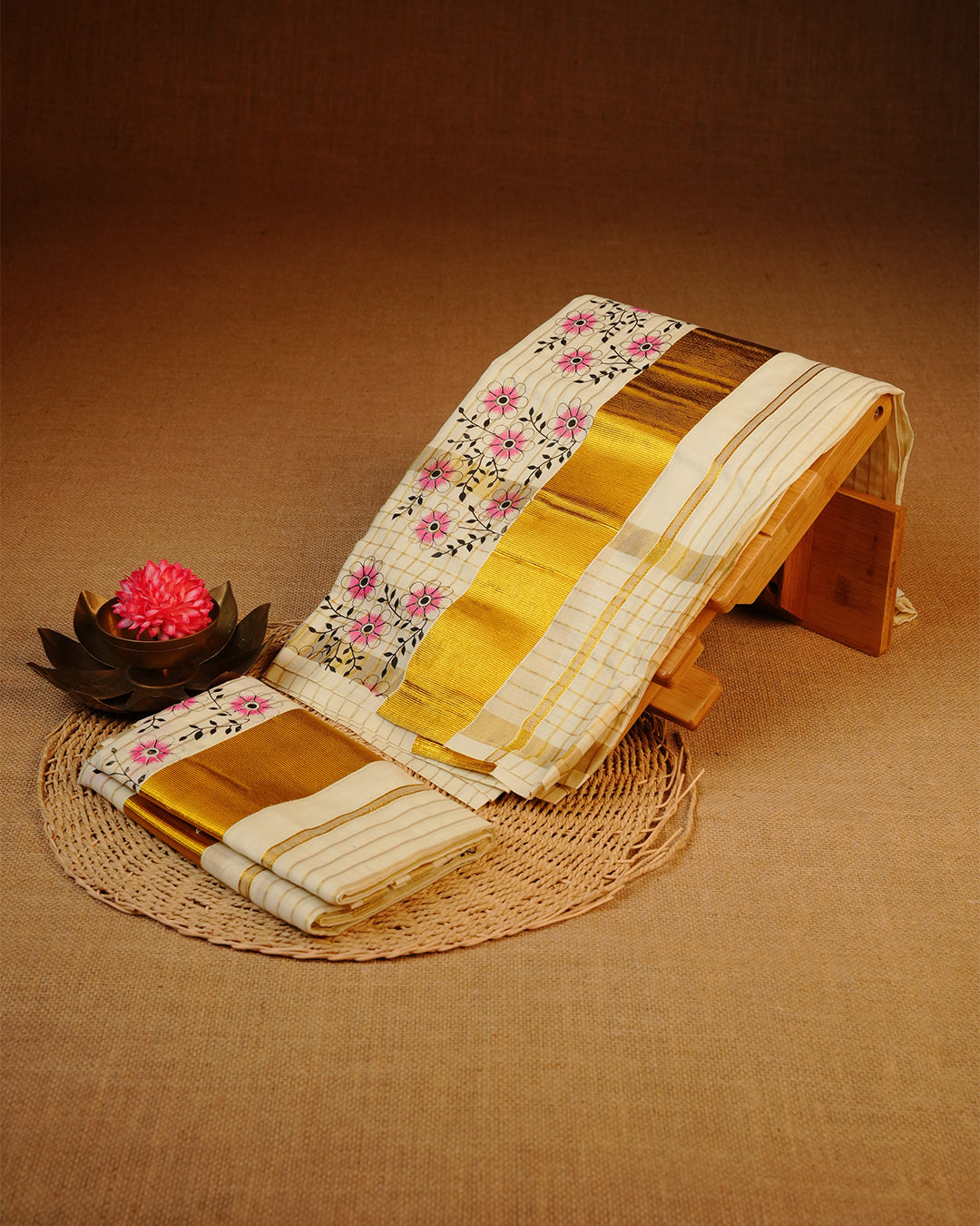 Cream colour cotton Set Mundu With Gold Zari stripes on body, enhanced with gold Kasav With Pink Floral Printed kara.