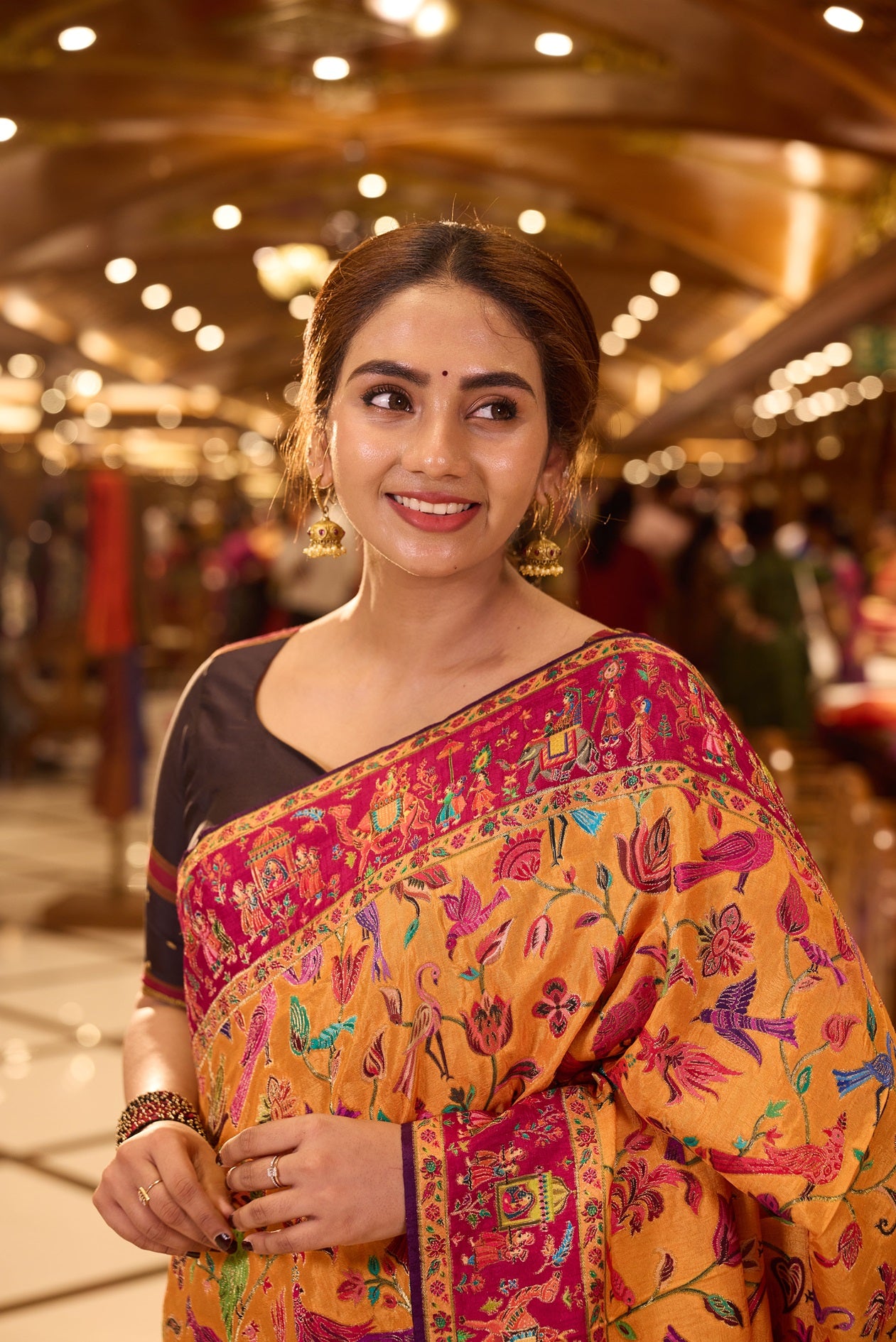 Mustard Yellow Pashmina Silk saree beautifully adorned with intricate multicolor floral and bird motifs woven across the body, complemented by a contrasting maroon border and paired with a matching blouse piece.