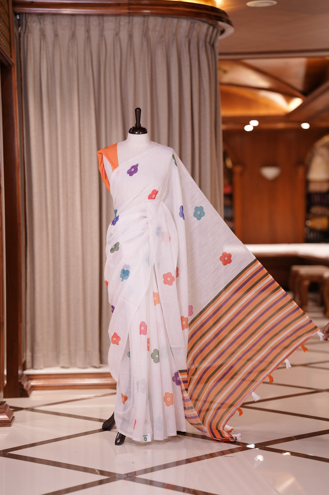 White colour Soft linen saree adorned with multiple floral digital prints all over, complemented by a contrast striped pallu & Paired with a beautifully contrasted printed blouse piece for an elegant contemporary look.