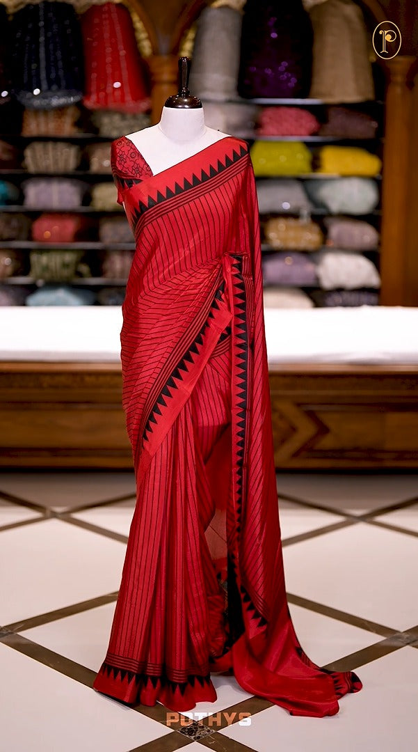 Red semi modal crepe saree featuring black vertical line prints, complemented by a temple border and circle butta design on the pallu, paired with a matching printed blouse.