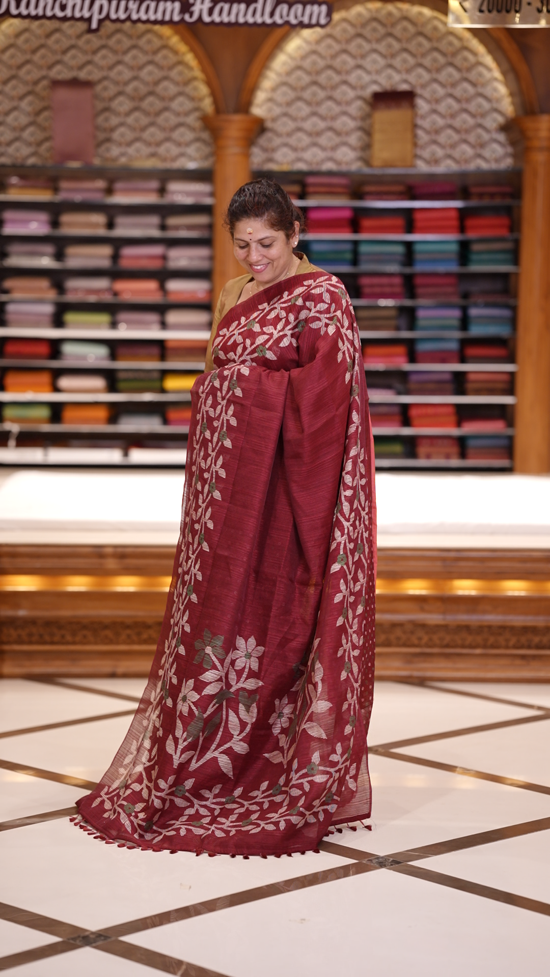 Maroon colour semi jute silk saree adorned with intricate floral and leaf motifs across the body & The pallu features detailed woven patterns enhancing its charm, paired beautifully with a matching floral printed blouse piece.
