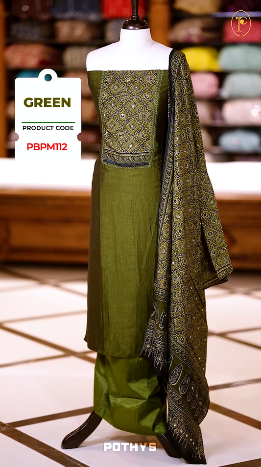 Green colour Ajrakh print semi silk churidhar material with intricately patterned top, mirror work highlights, printed dupatta with detailed border, and plain bottom perfect for elegant festive and casual wear.