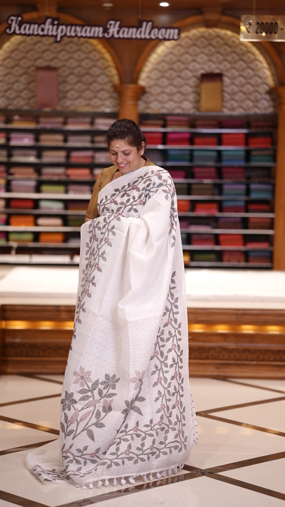 White colour semi jute silk saree adorned with intricate floral and leaf motifs across the body & The pallu features detailed woven patterns enhancing its charm, paired beautifully with a matching floral printed blouse piece.