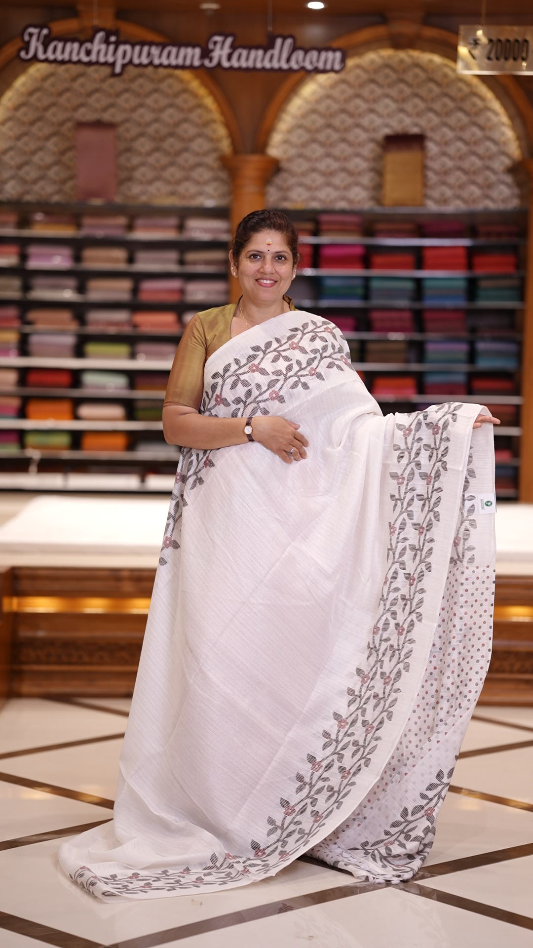 White colour semi jute silk saree adorned with intricate floral and leaf motifs across the body & The pallu features detailed woven patterns enhancing its charm, paired beautifully with a matching floral printed blouse piece.