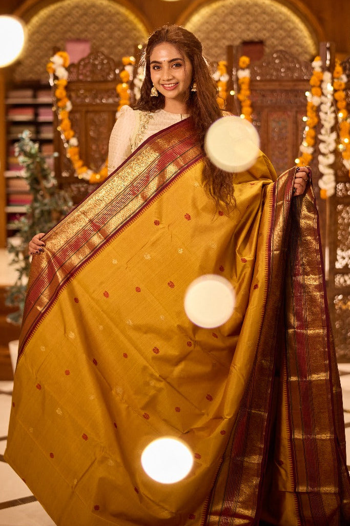 Pure silk saree featuring a mustard yellow body adorned with small zari and thread motifs, complemented by a rich maroon zari woven border and grand pallu.