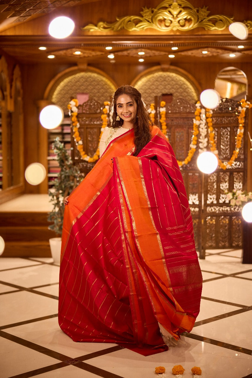 Pure silk saree featuring a rich red body with golden zari stripes, contrasted by an orange pallu and finely woven zari border.
