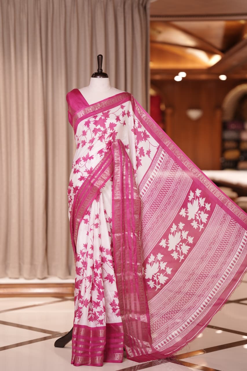 White colour semi tussar silk saree adorned with Pink floral prints, highlighted by Pink Colour traditional border Paired with a matching blouse and a beautifully printed pallu for classic elegance.