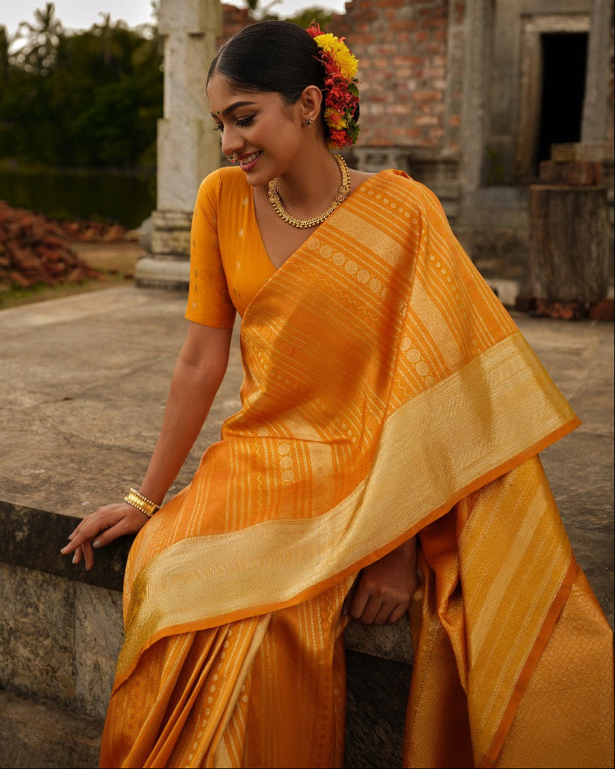 Golden mustard colour Samudrika wedding saree featuring elegant vertical geometric jacquard designs woven in antique silver and copper zari, complemented by a traditional zari pettu border and paired with a matching blouse piece.