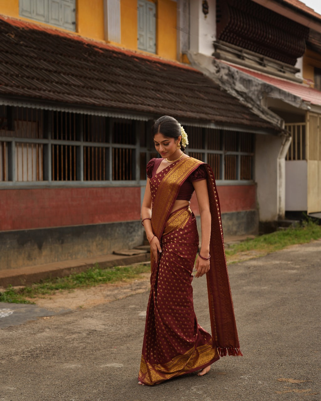 Dark brown colour Samudrika Pattu saree featuring traditional round motifs with antique silver zari Meenakari weaving across the body, beautifully complemented by a classic heritage gold zari border and paired with a matching blouse piece.