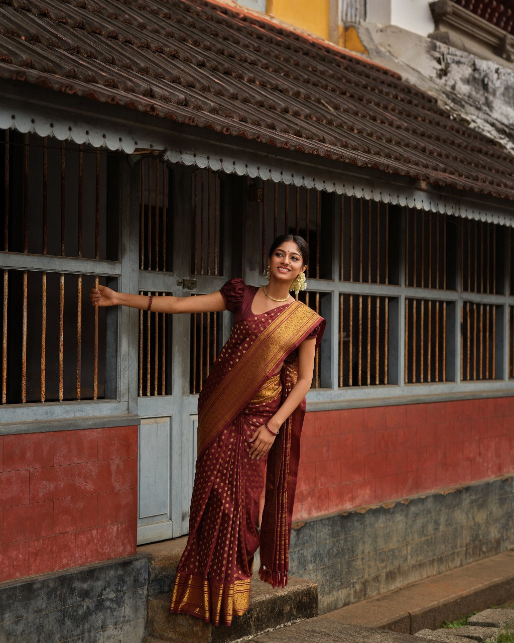 Dark brown colour Samudrika Pattu saree featuring traditional round motifs with antique silver zari Meenakari weaving across the body, beautifully complemented by a classic heritage gold zari border and paired with a matching blouse piece.