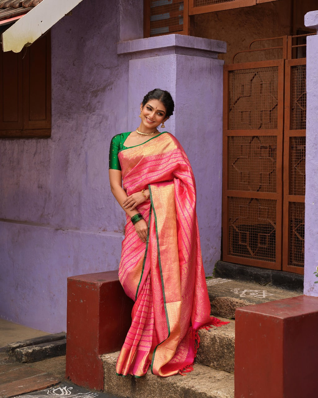 Rani pink colour Samudrika Pattu saree featuring elegant horizontal zari jacquard weaving, complemented by a traditional gold zari border accentuated with green piping for a striking finish, and paired with a matching blouse piece.
