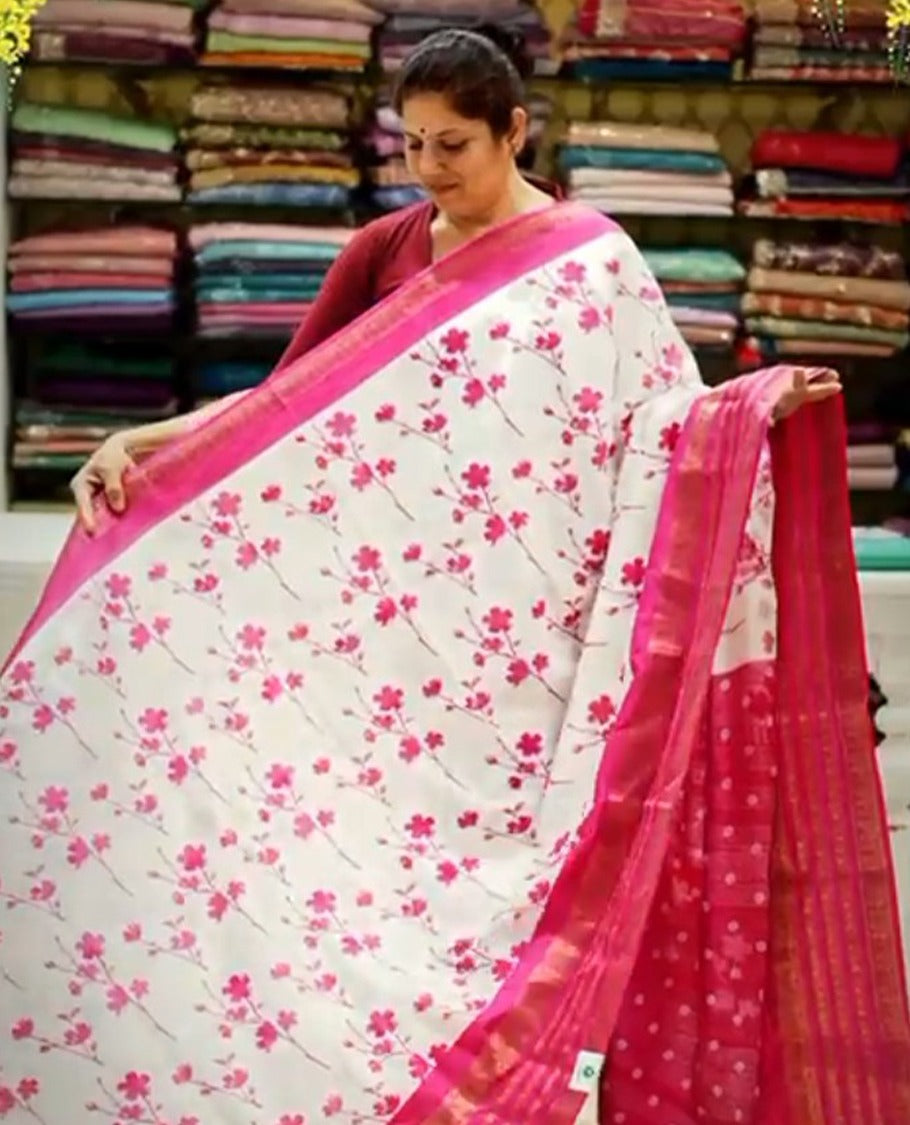 Cream colour semi tussar silk saree featuring magenta floral print on body, contrast magenta colour gold zari border, paired with matching blouse piece.