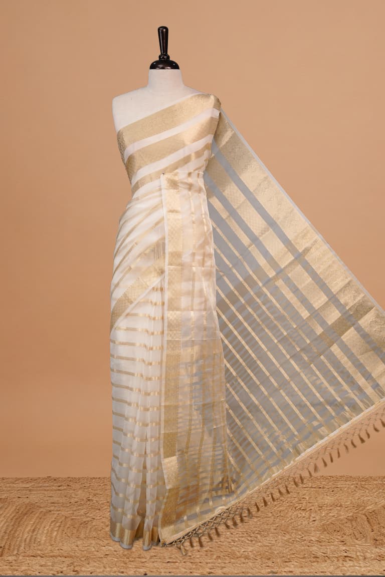 White Colour Semi Organza Saree Featuring Elegant Gold zari Stripes Detailing on body, Traditional border, comes with matching blouse piece.