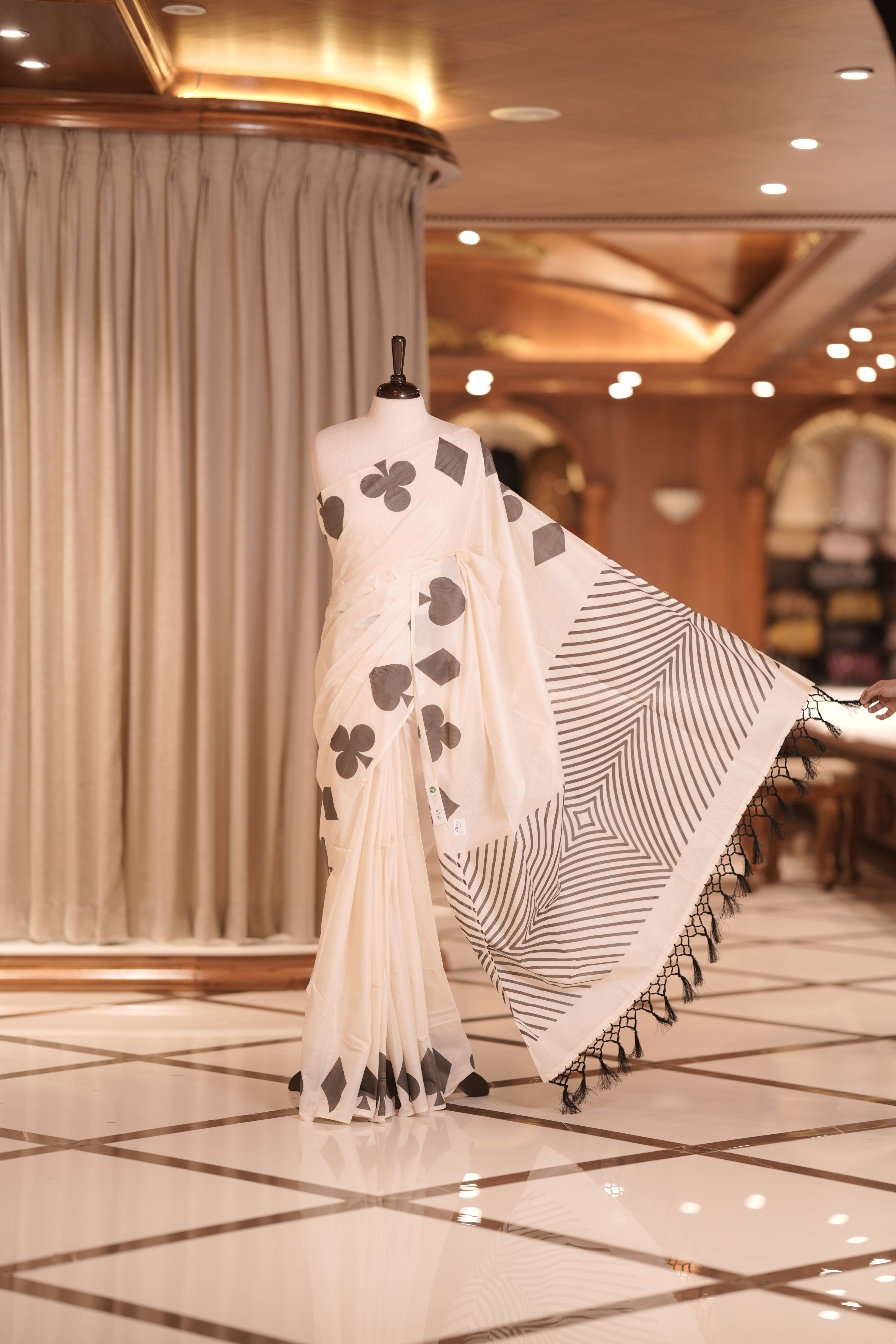 Off white colour kerala cotton saree adorned with black colour card suit motifs , The pallu features striking zigzag patterns with tassel detailing, creating a perfect fusion of tradition and modern sophistication.
