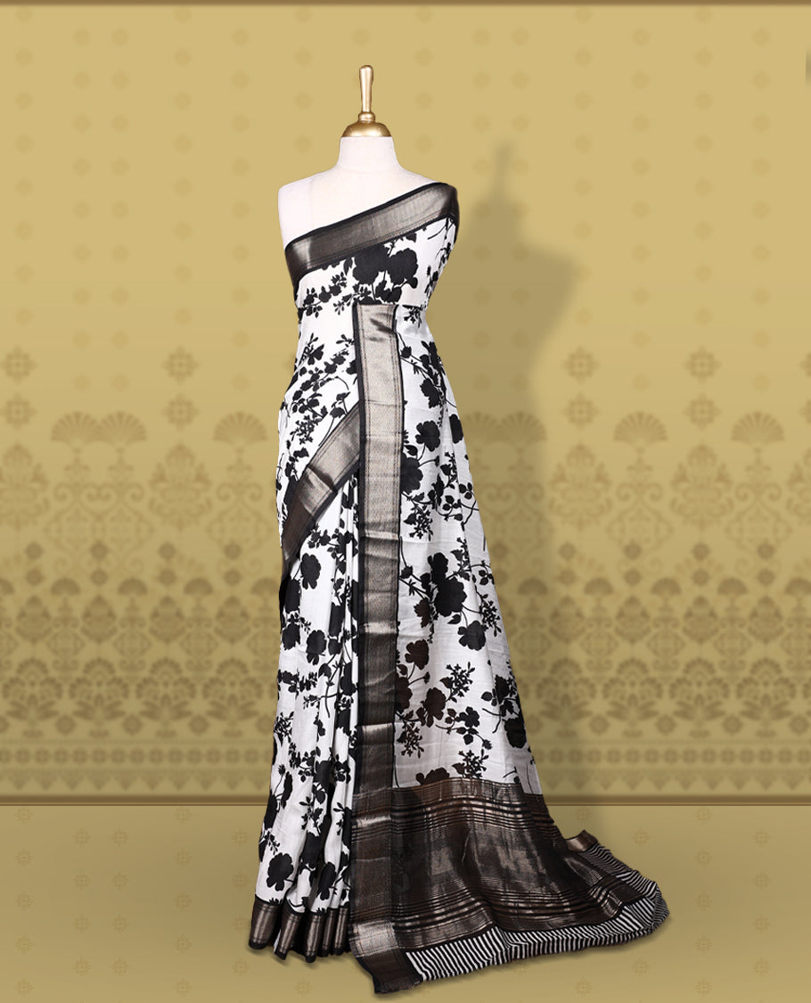 White colour saree adorned with bold black floral prints and a rich black zari border and stripped checkered pallu & Comes with a matching blouse piece.