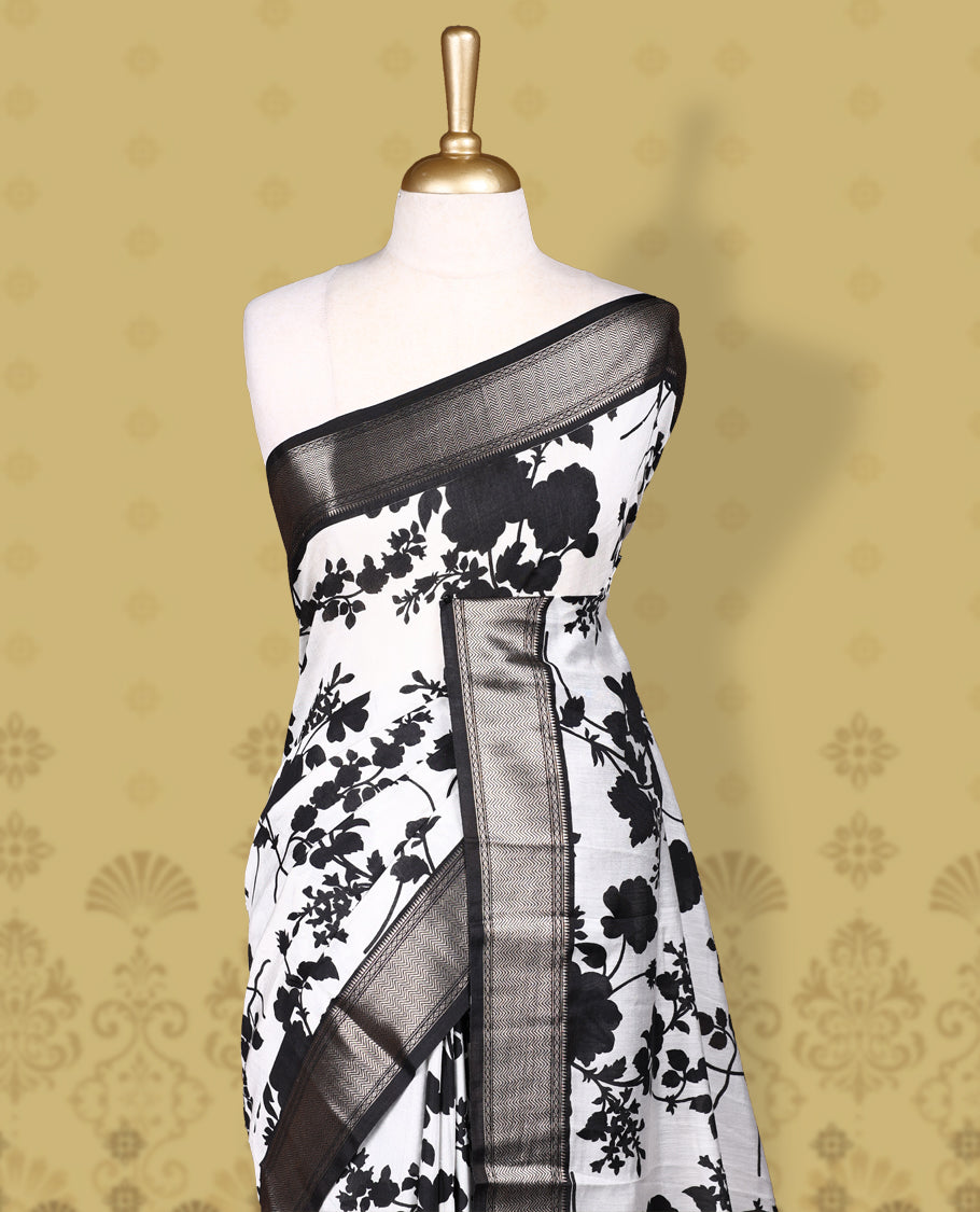 White colour saree adorned with bold black floral prints and a rich black zari border and stripped checkered pallu & Comes with a matching blouse piece.