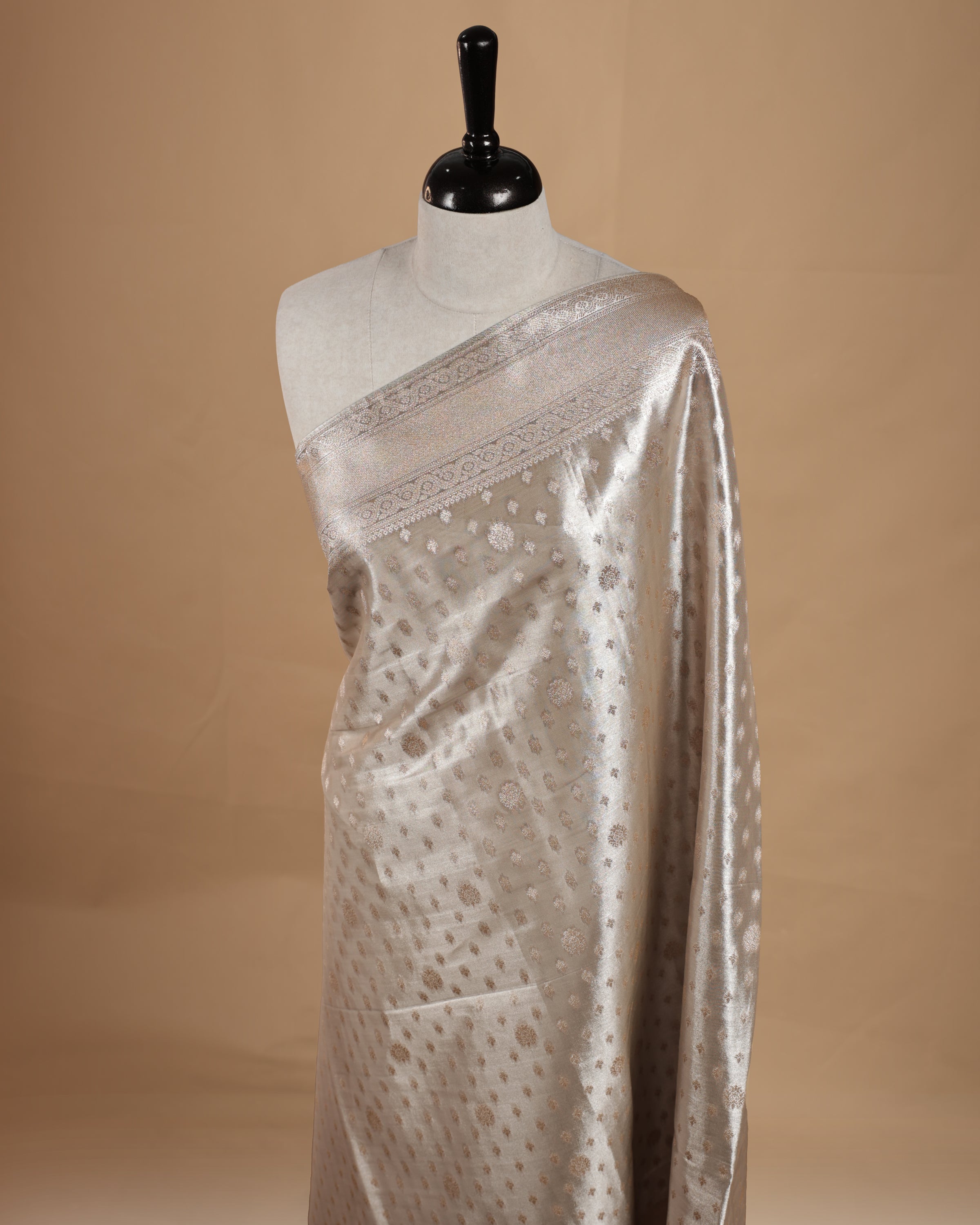 Pastel grey colour semi tissue silk saree featuring floral zari motifs on body, complemented by gold zari traditional border, paired with matching blouse piece.