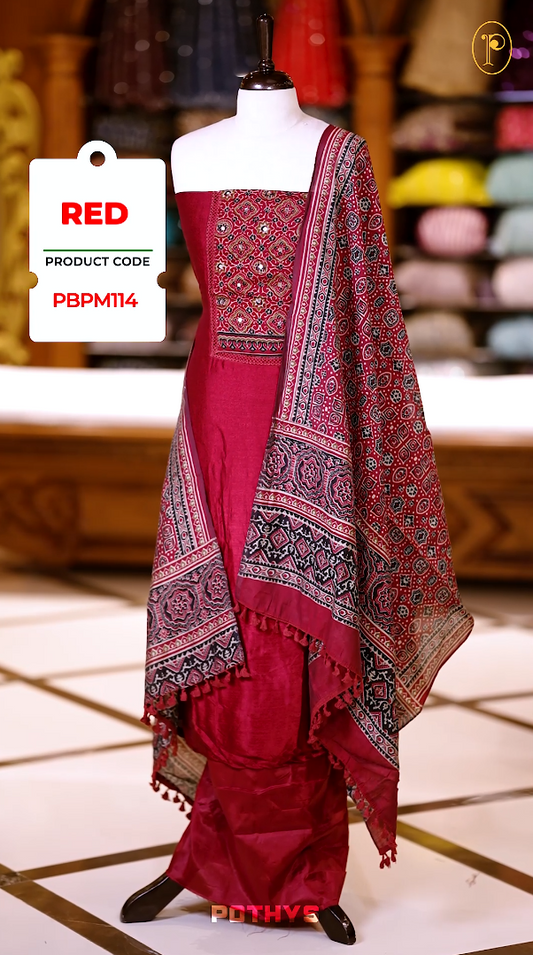 Red colour Ajrakh print semi silk churidhar material with intricately patterned top, mirror work highlights, printed dupatta with detailed border, and plain bottom perfect for elegant festive and casual wear.