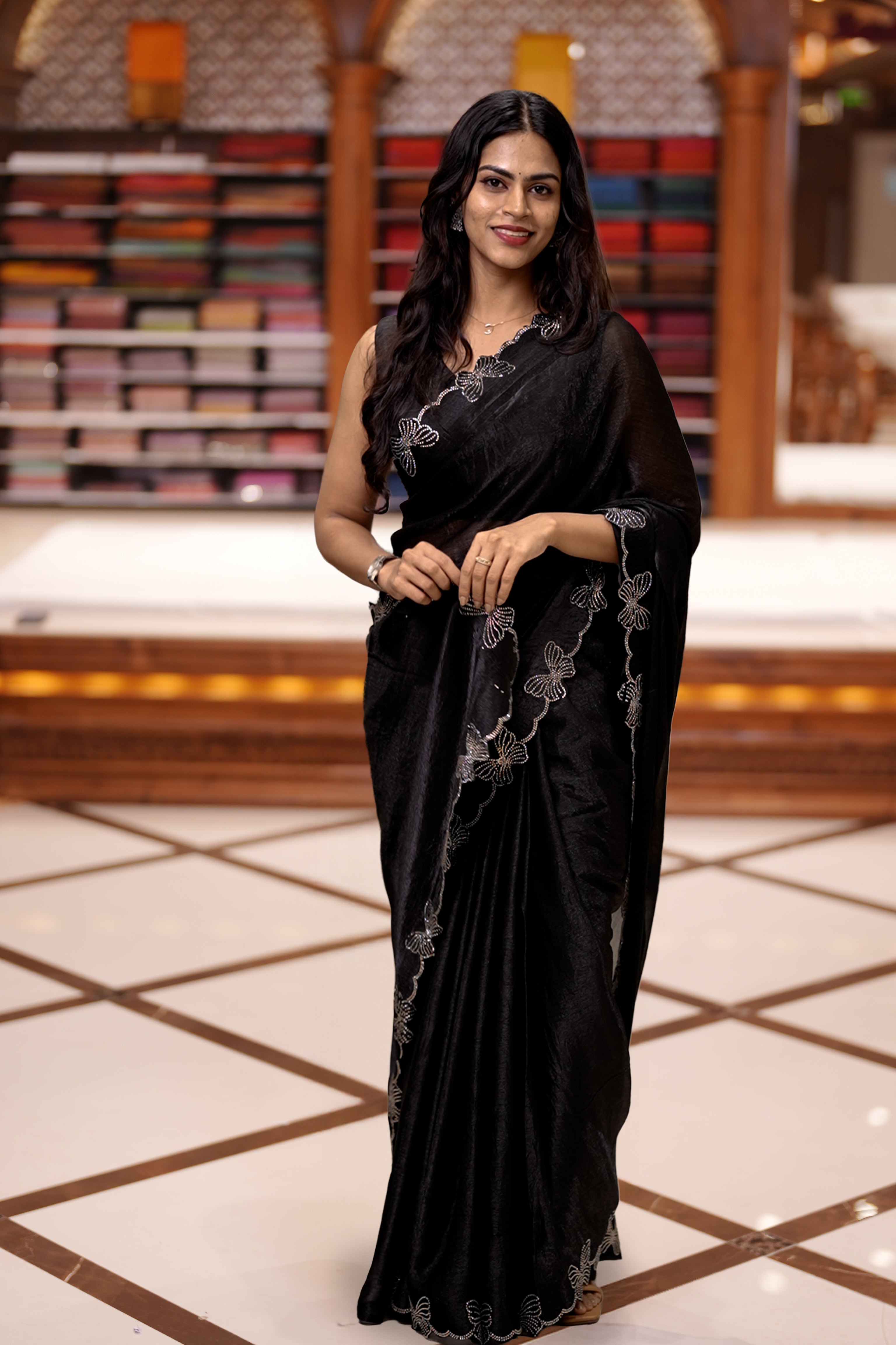 Black colour chiffon saree adorned with Swarovski stone butterfly designs along the side border, adding a touch of sparkle, Paired with a matching blouse piece featuring the same intricate stone work.
