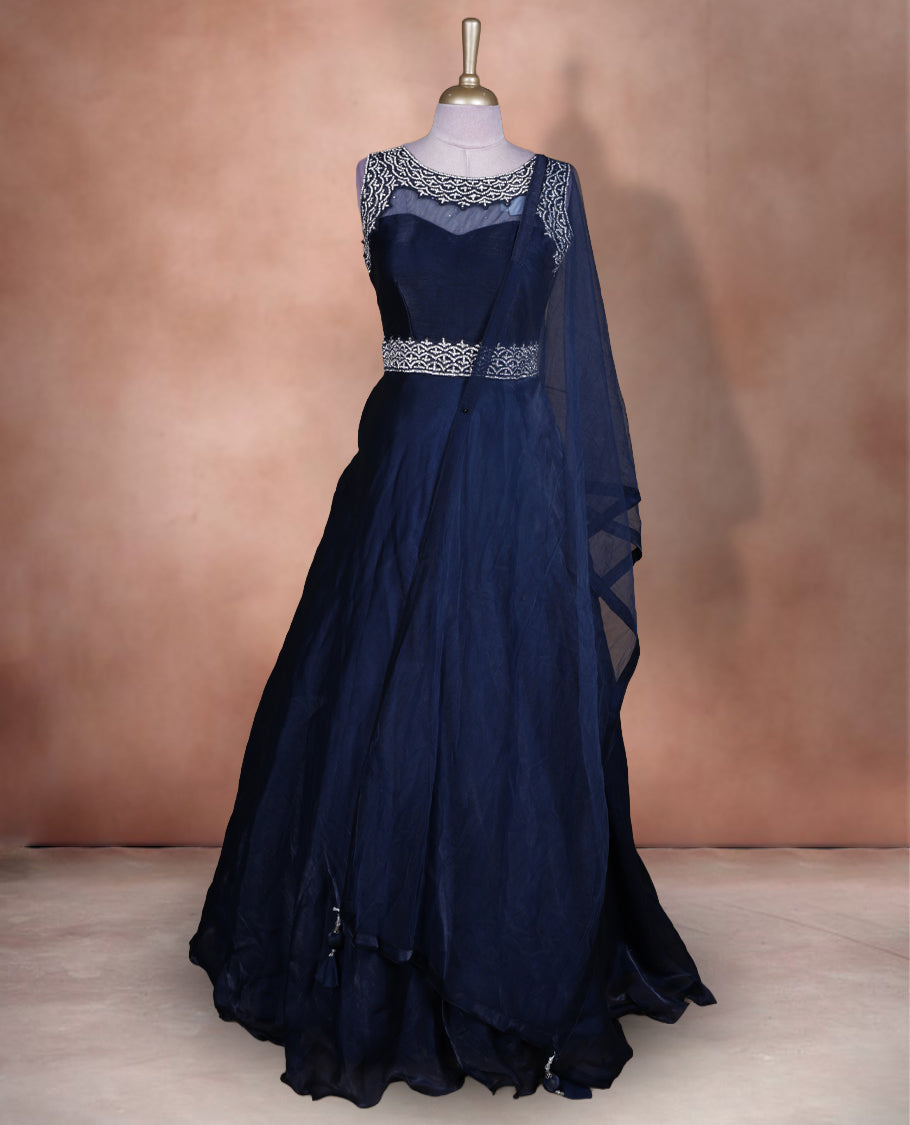 Navy blue colour Gown with stitched sleeveless embellished blouse featuring sheer yoke and waist detailing, matching stitched flared lehenga with tassel accents, and plain sheer dupatta.