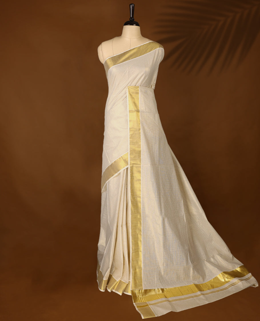 Elegant off white colour cotton Kerala saree featuring Tiny Checked body, gold zari traditional kasavu border offering a classic and graceful look, paired with a matching blouse.