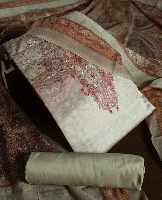 Beige colour churidhar material with subtle paisley motifs, sequin highlights, and woven border design, paired with a plain matching bottom and a soft printed dupatta for a graceful ethnic look.