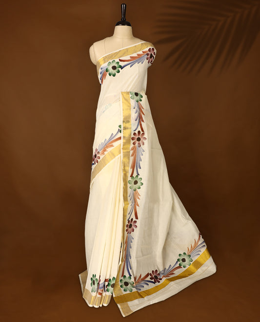 Elegant Off White Colour Kerala Cotton Saree adorned with hand painted floral motifs in earthy tones,Highlighted with a classic Gold Kasavu border and matching blouse, perfect for festive and traditional occasions.