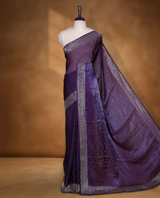 Dark purple colour chiffon designer saree, featuring dainty scattered stones on the body, enriched with dense stone work and a heavy metallic stone border and pallu, paired with a matching blouse.