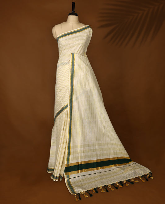 Elegant off white colour cotton Kerala saree featuring subtle golden checks, green & gold zari border, and rich striped pallu with tassels, offering a classic, graceful look &Pair with a matching blouse for charm.